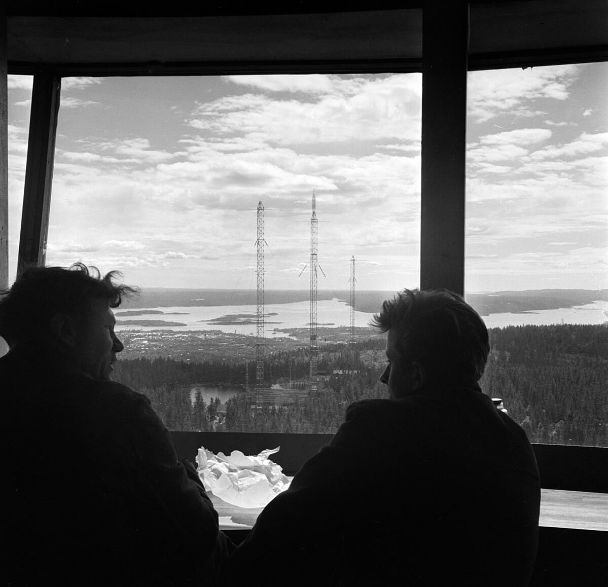 Arbeidere tar en pause i Tryvannstårnets øverste etasje og nyter den spektakulære utsikten over Oslo og Tryvannsmastene. Tryvannstårnet har vært et viktig landemerke og symbol på Oslo siden 1962